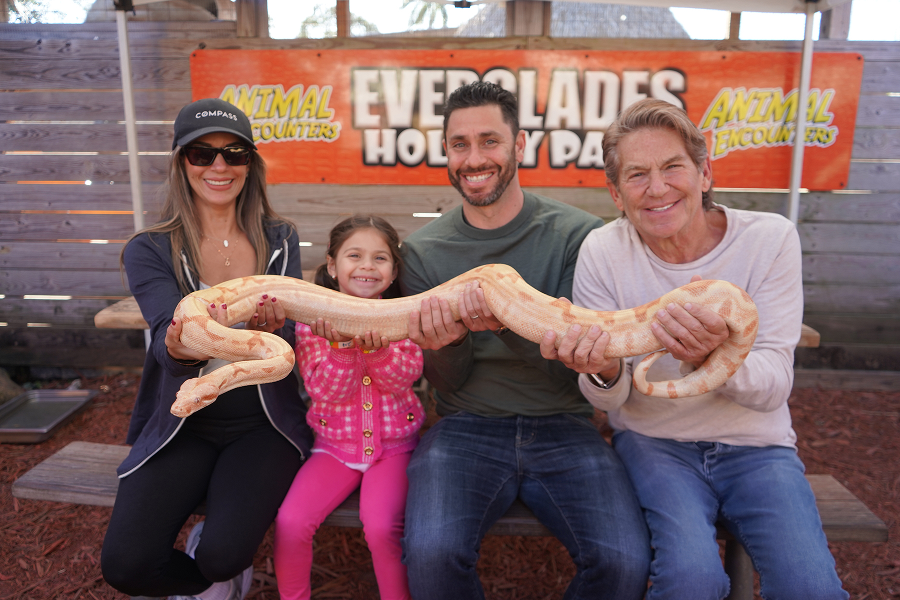 Four people holding a large snake, smiling in front of a sign.