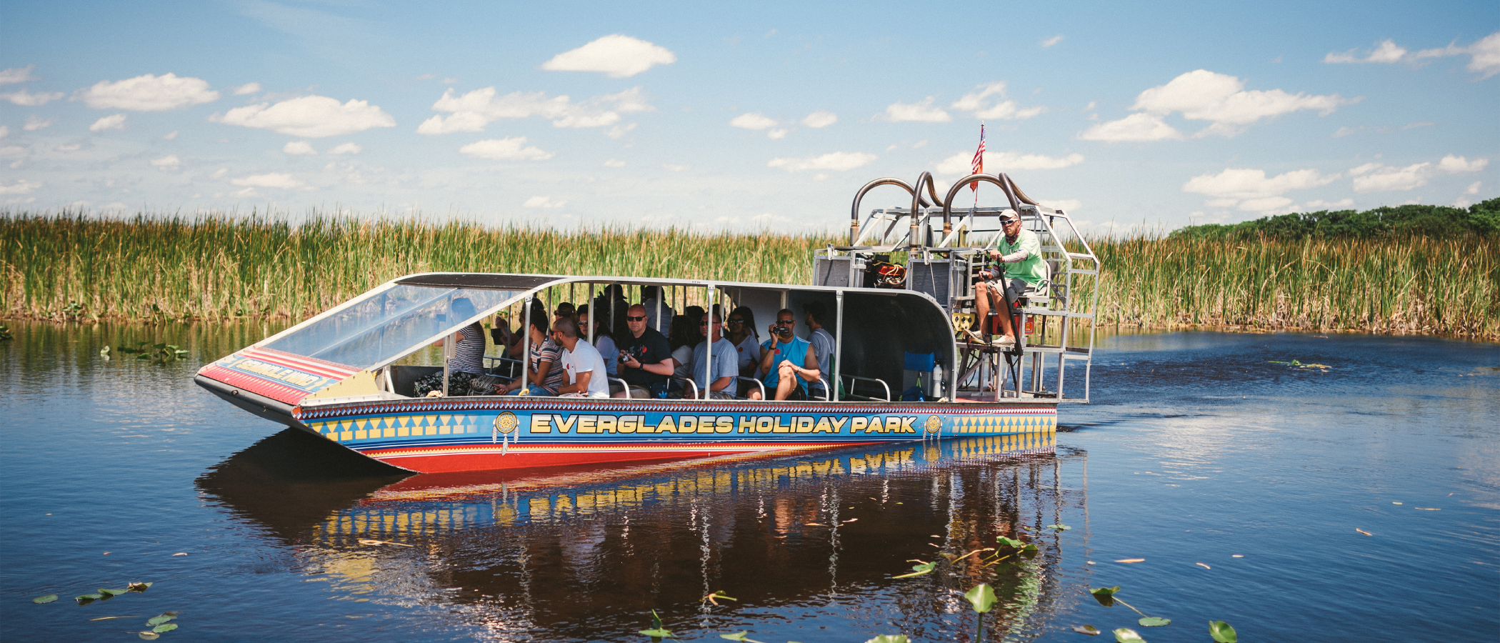 Airboat with tourists on a marshy waterway surrounded by reeds.