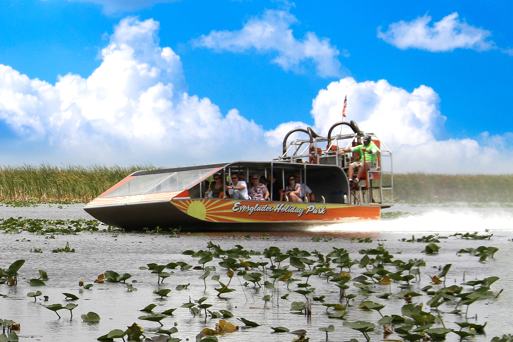 Airboat gliding through wetlands with passengers under a blue sky.