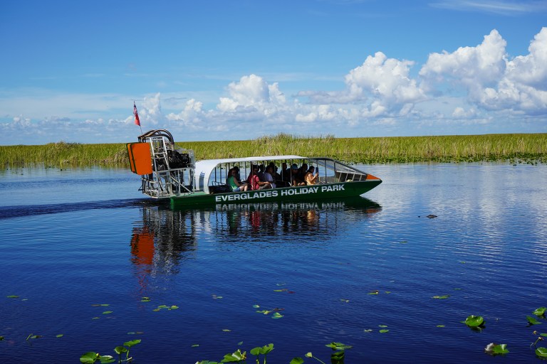 Airboat on a calm river at Everglades Holiday Park under a partly cloudy sky.