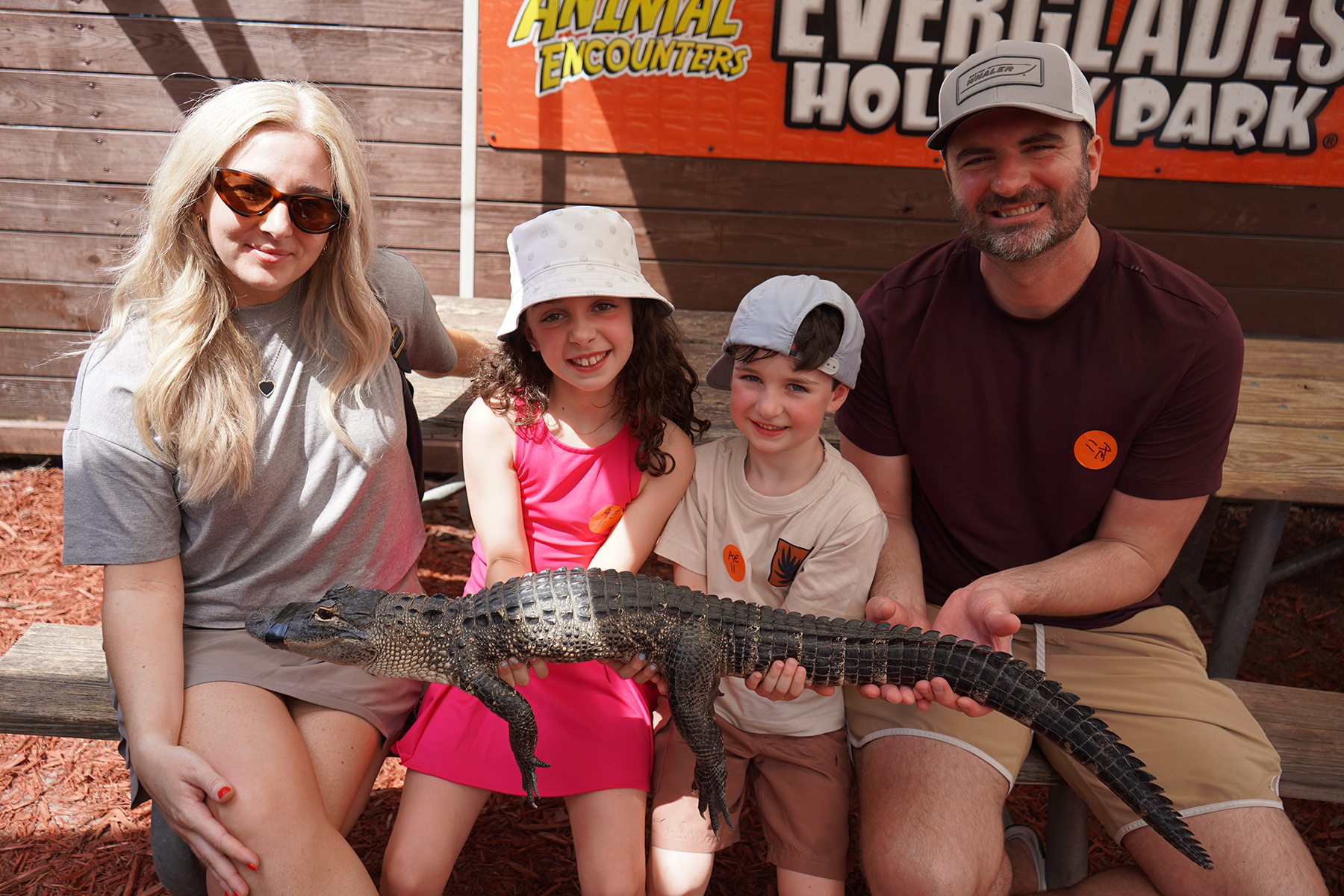 Family sitting on a bench holding a small alligator at a wildlife park.