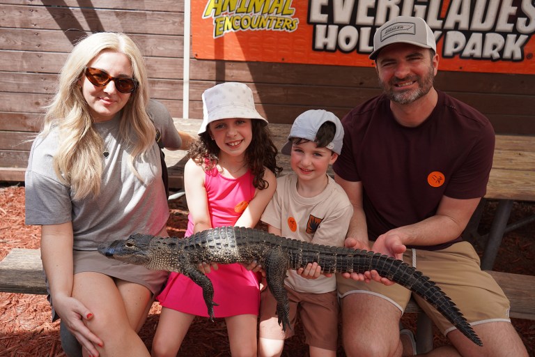 Family sitting on a bench holding a small alligator at a wildlife park.