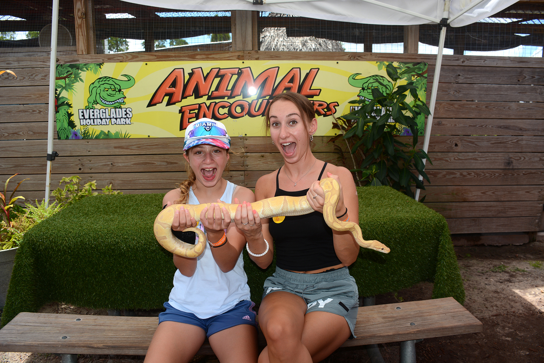 Two people excitedly holding a snake in front of an 'Animal Encounters' sign.