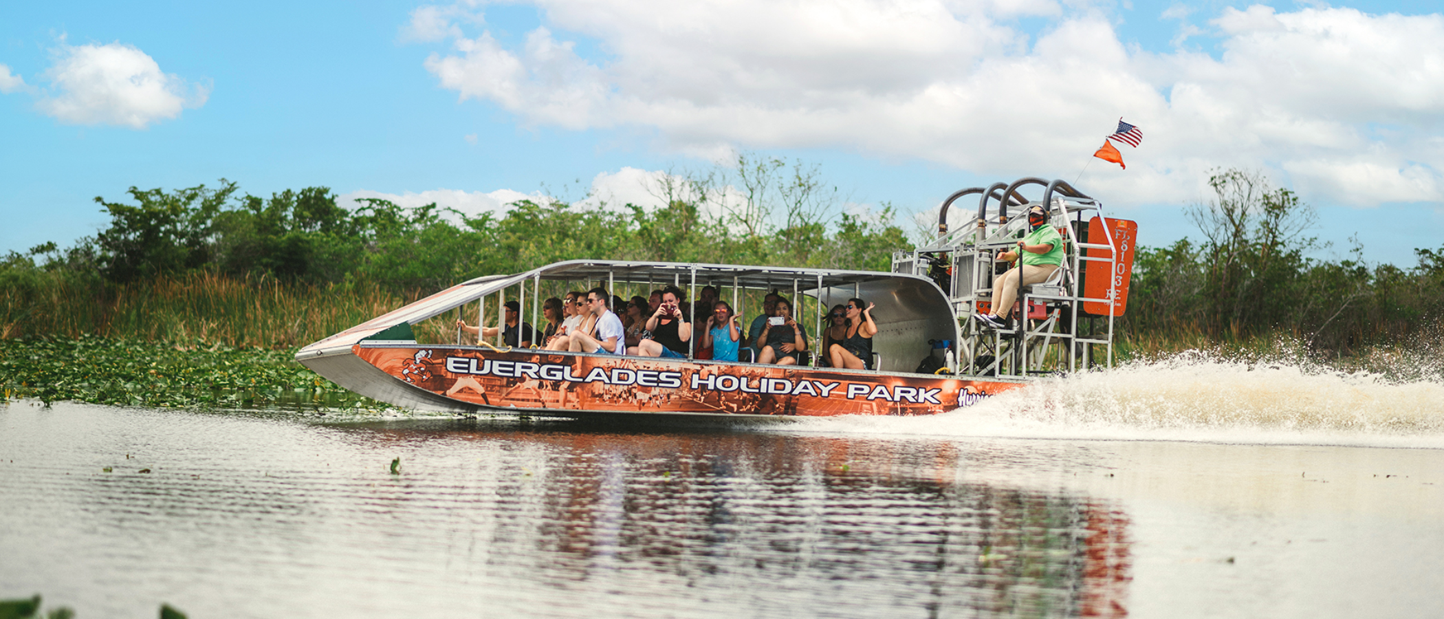 Airboat with passengers cruising in a wetland area, surrounded by greenery.