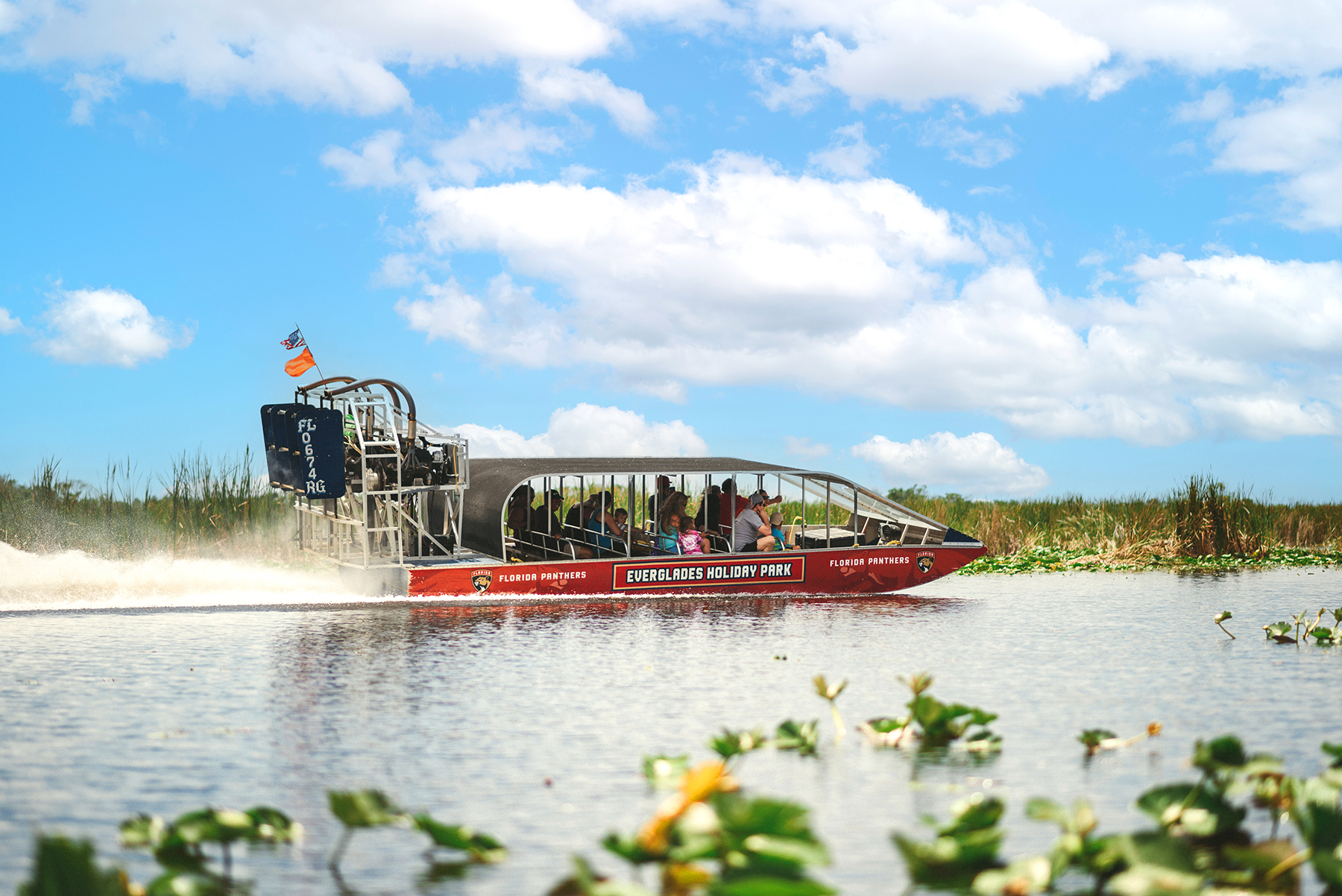 Airboat with passengers gliding on a waterway under a blue sky.