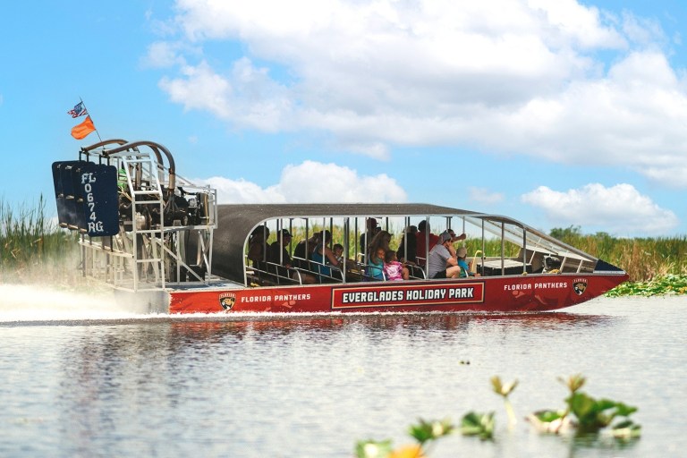 Tourists in airboat at Everglades Holiday Park under blue sky.